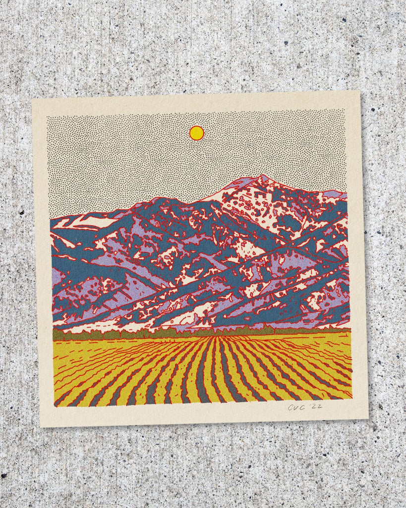 Another postcard featuring a blue and purple mountain with a field of greenish yellow crops in the foreground. The sky is white with tiny black dots and a larger yellow dot for the sun. 