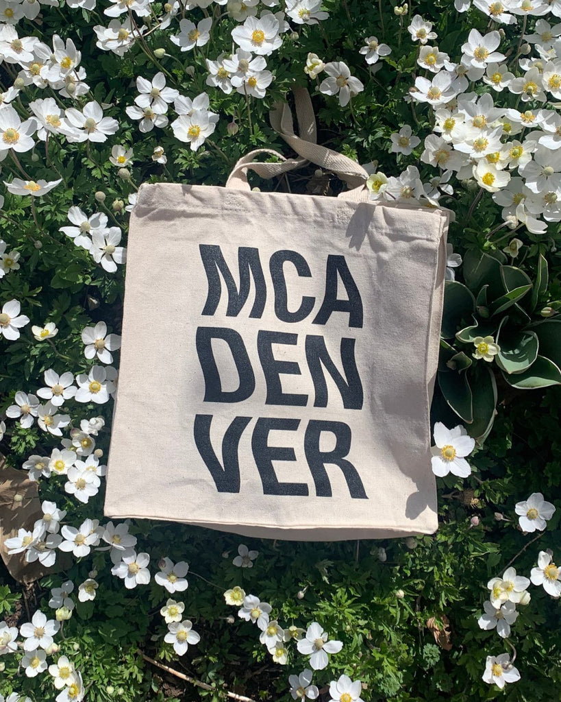 MCA Denver Wavy Tote on a bed of green and white flowers. 
