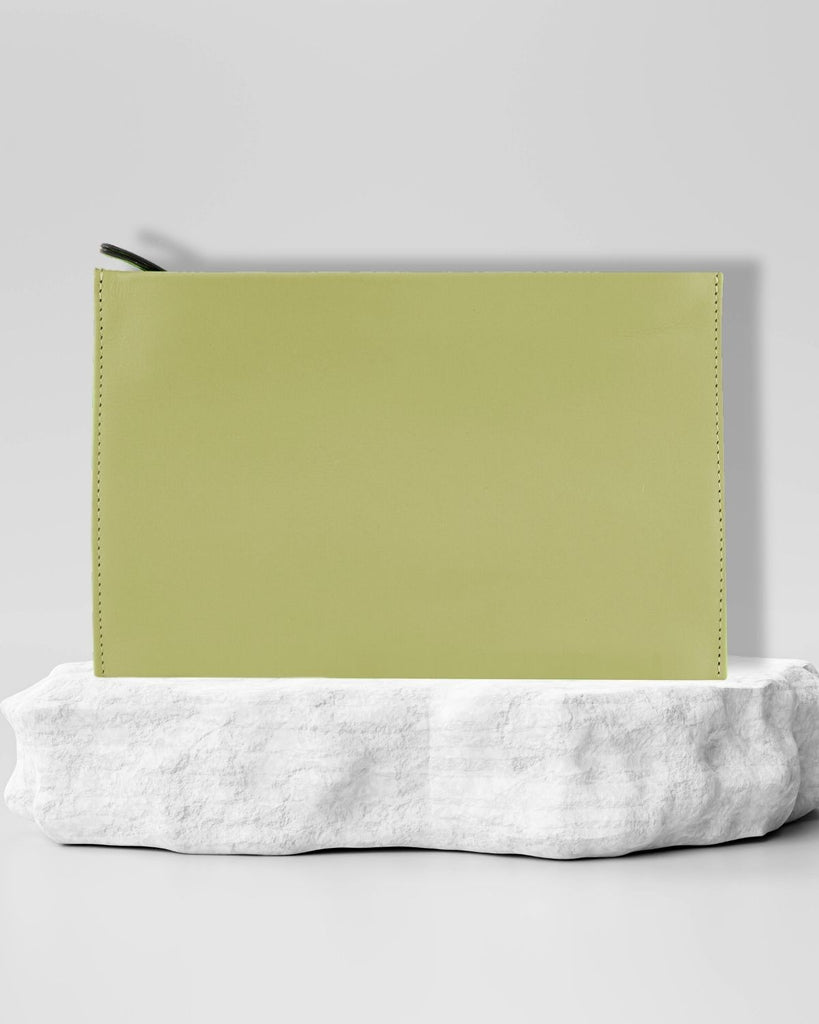Handmade leather pouch. A rectangle shape with zipper closure. Pale green leather and stitching. The pouch sits on a marble pedestal. 