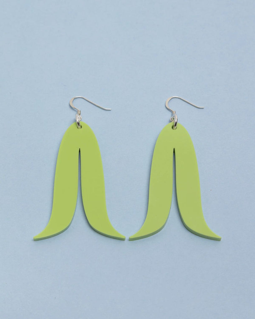The Sour Apple earrings against a light blue surface.  The earrings are a pastel green color and have a double leaf-like shape. 