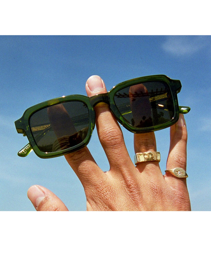 A hand holds the sunglasses up to the blue sky. 