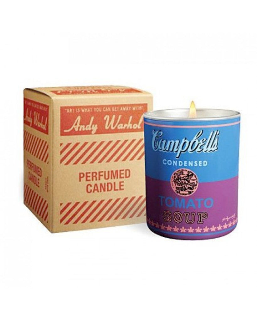 Candle shown with the box it comes in against a white backdrop. The candle is blue on top and purple on bottom. The box is situated a bit behind the candle and has text in red that reads 'Andy Warhol' 'Perfumed Candle'