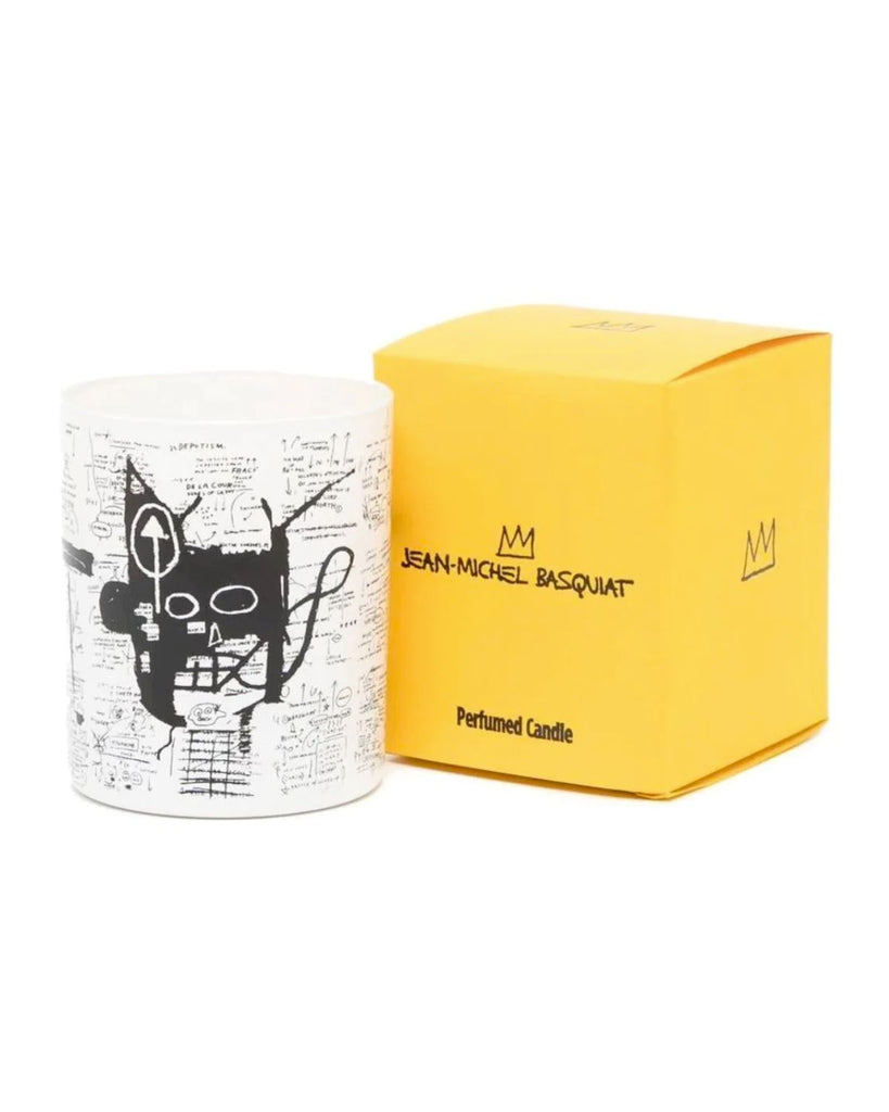 The candle is shown with the box it comes in against a white backdrop. The Candle is white and has a famous work of art by Basquiat on the front in black. The Box is yellow and is situated a bit behind the candle. The text on the box reads 'Jean-Michel Basquiat' 'Perfumed Candle'