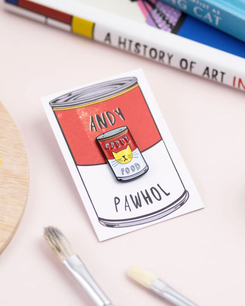 Andy Warhol inspired cat pin. Pin is in the shape of a Campbell's soup can and spells out 'Kitty Food' on it. In the center of the can is a cats face in yellow.  