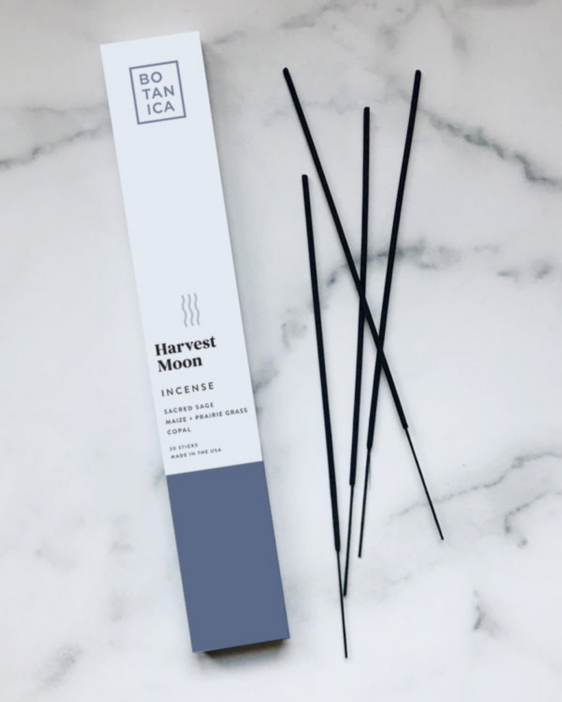 Incense packaging with incense sticks laid out beside it. The packaging is white with slate blue color on the bottom
