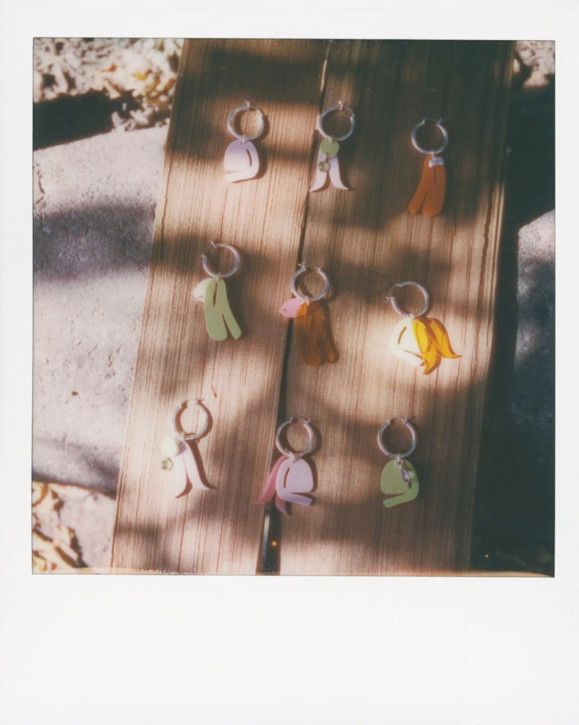 A polaroid photo of 9 different styles of earrings laid out on a wood slab. 