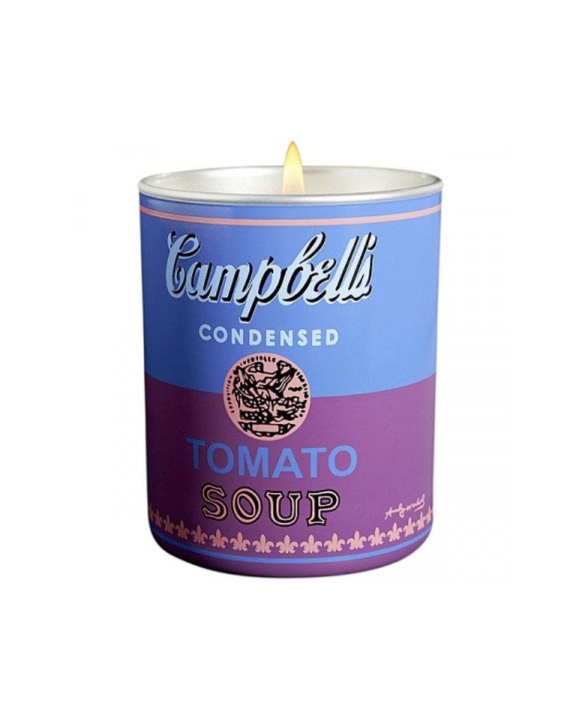 Candle is shown lit with a flame against a white backdrop. The candle resembles the famous Warhol soup cans. Blue on top and purple on bottom. 