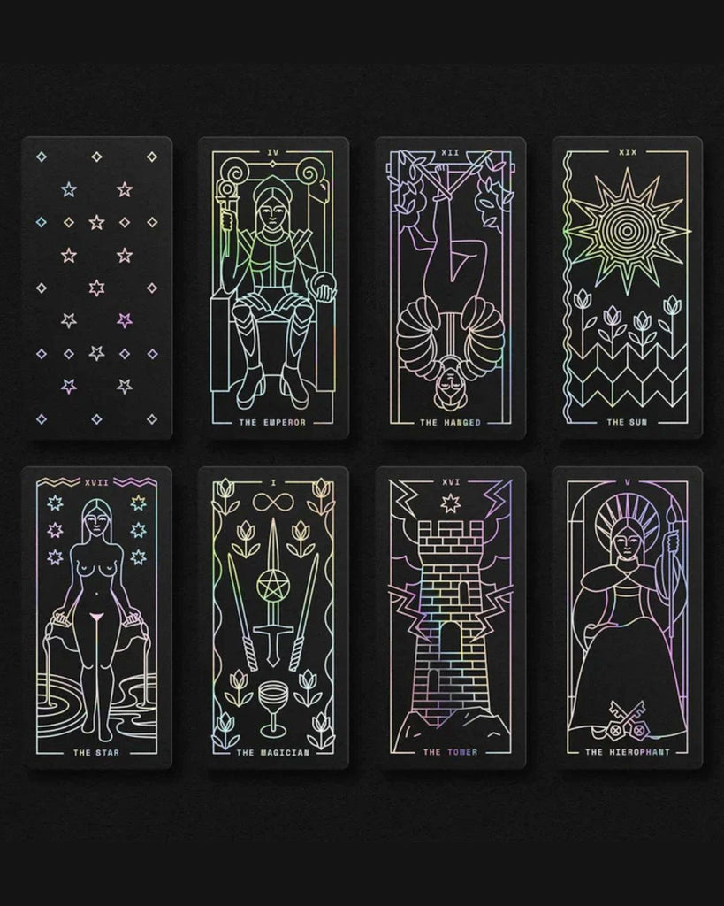A view of various tarot cards lined up against a black surface. The cards on black with holographic foil imagery and text. The front of the cards are black with holographic stars.  