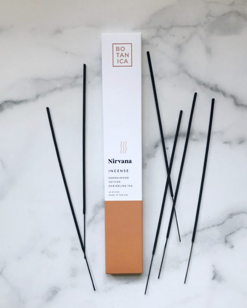 Incense packaging with incense sticks laid out beside it. The packaging is white with a burnt orange color on the bottom.