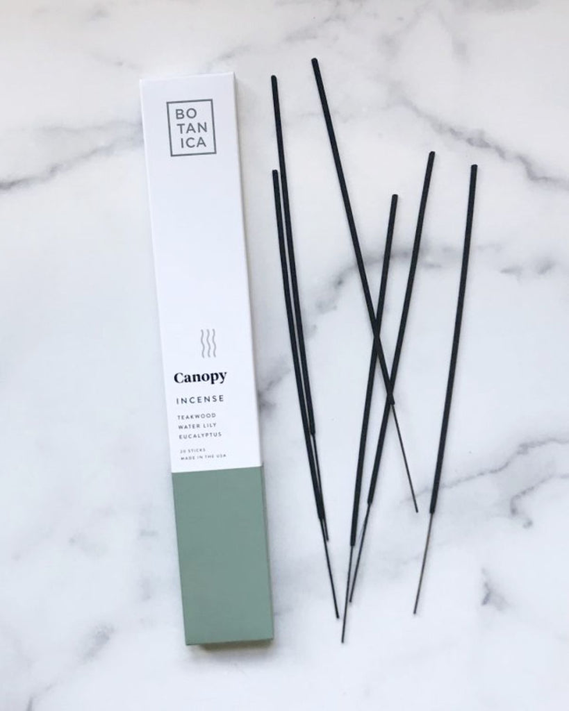 Incense packaging with incense sticks laid out beside it. The packaging is white with a greyish green color on the bottom.  