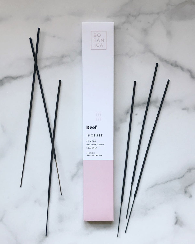 Incense packaging with incense sticks laid out beside it. The packaging is white with a soft light pink color on the bottom.  