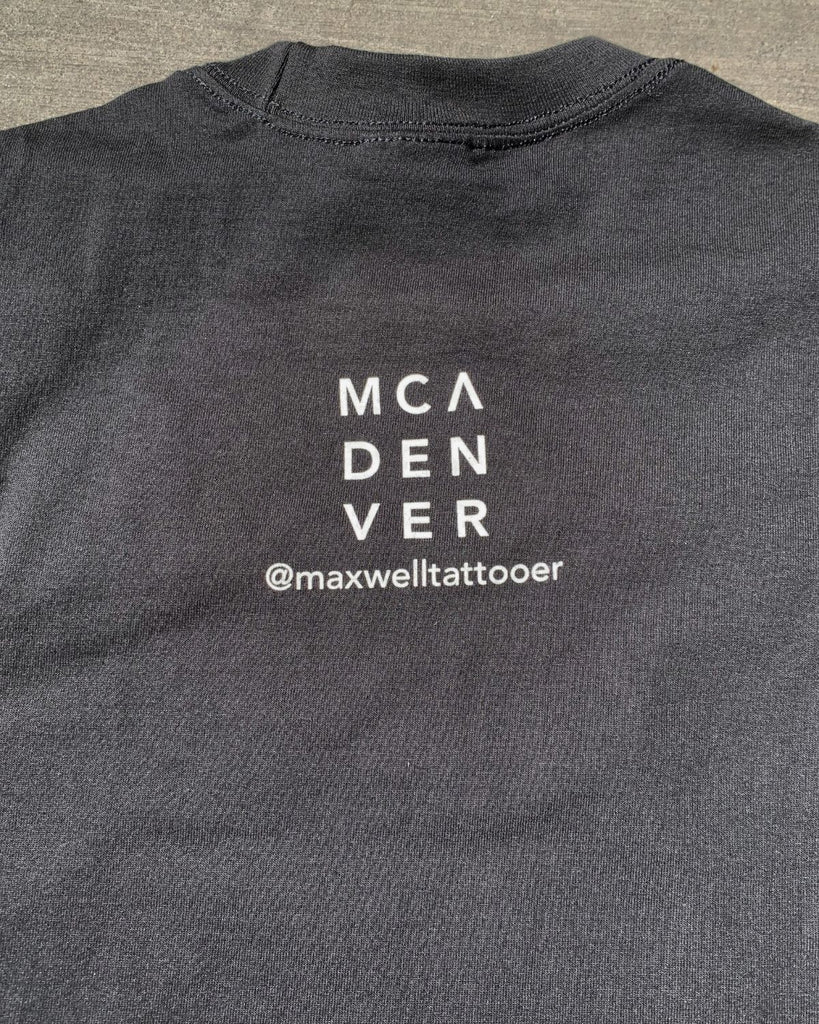 The back nape of the t-shirt that has our  'MCA Denver Logo' and the artists instagram name 'maxwelltattooer'