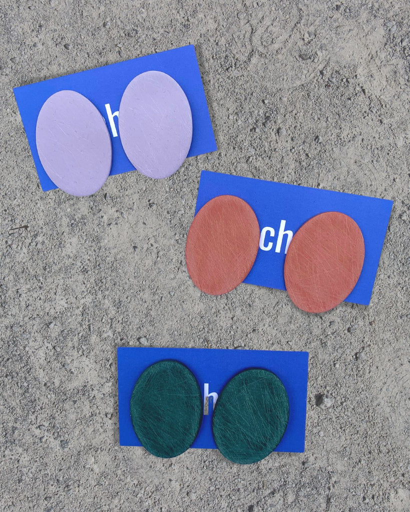 Three different color ways of the earrings laid out on cement. Lavender is on top, Dusty Rose in the middle, and Emerald Green on the bottom.