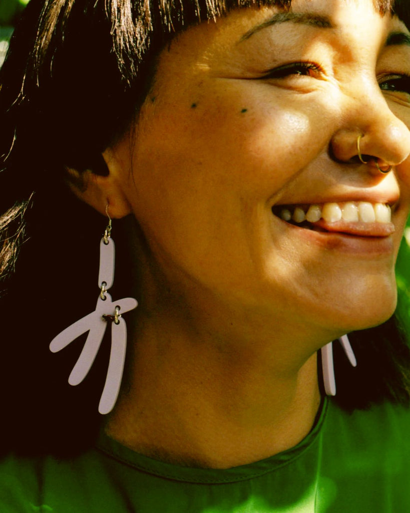 Model wearing the Lilac earrings caught in mid laugh. She's wearing a green shirt and has short dark brown hair. 