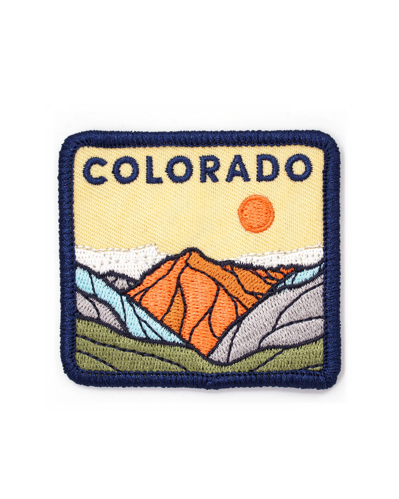 Colorado embroidered patch made right here in Denver! The patch shows a mountain scape scene with an orange sun in the sky. On top of the mountains reads 'Colorado' in embroidered letters. 