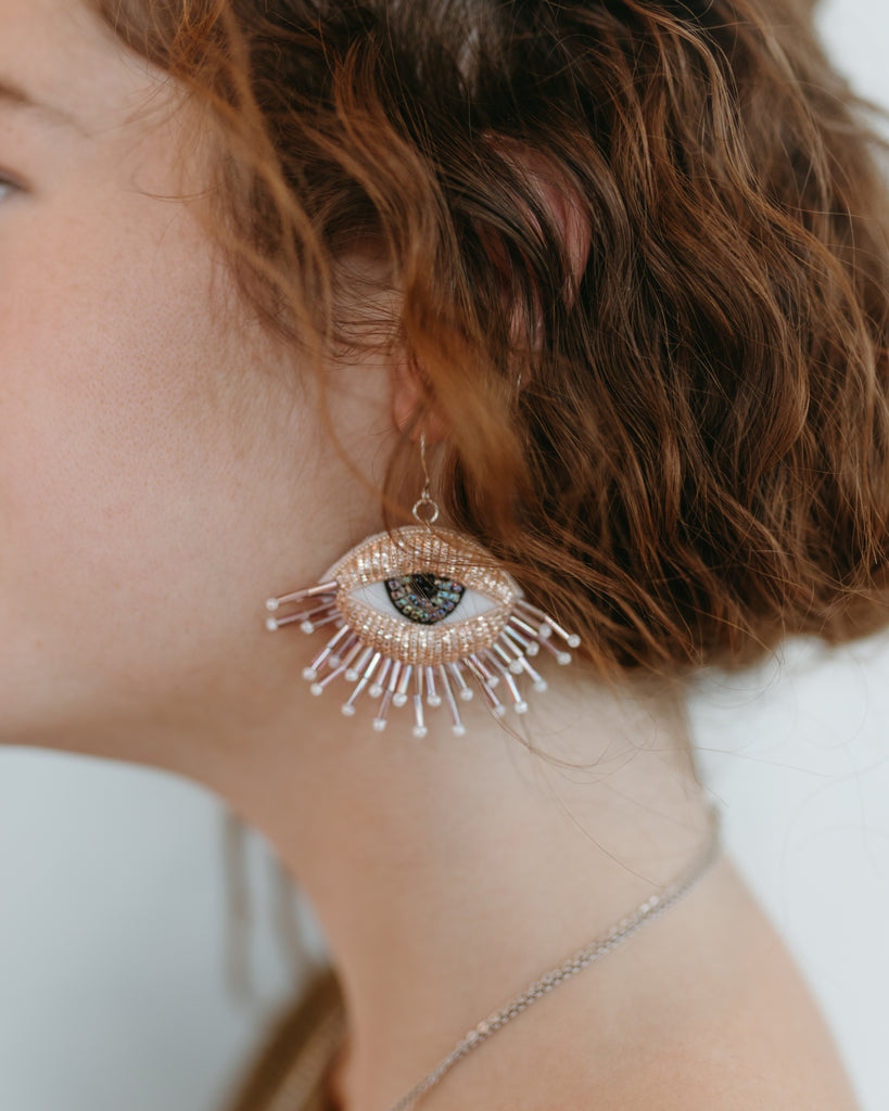 Eye earrings shown peeking from reddish brown hair on model, Meredith. 