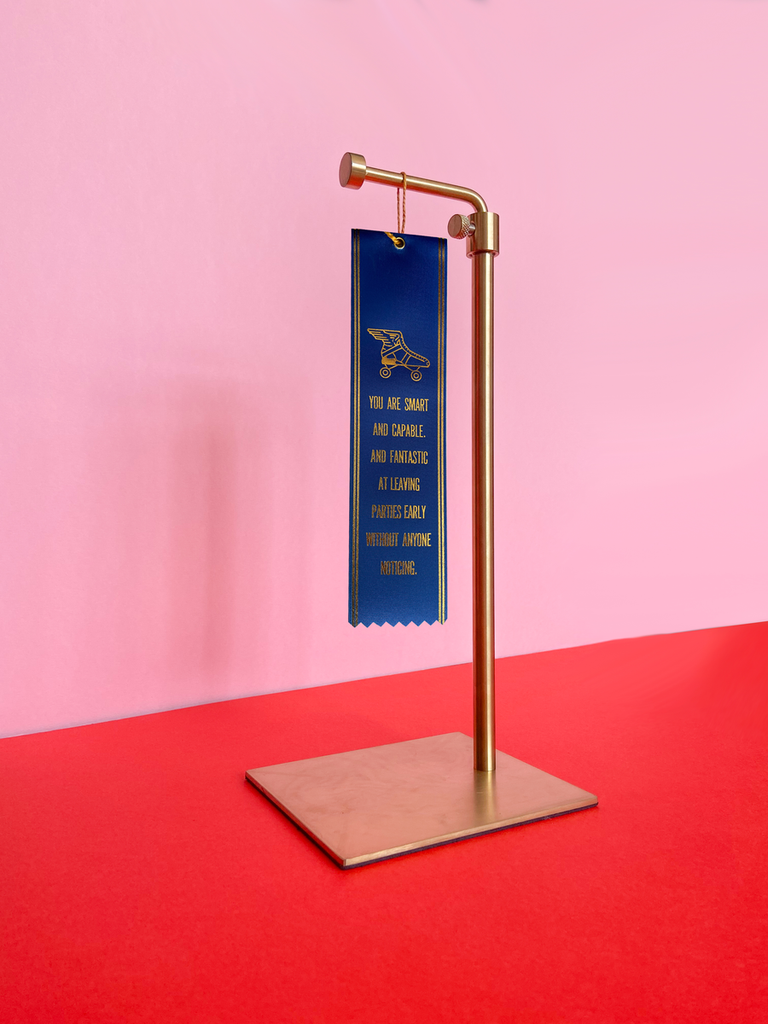 The ribbon hanging from a gold stand. The surface is red and the wall behind it is pink. 